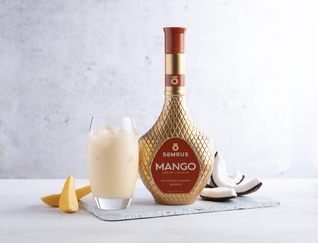 Mango flavoured alcoholic cream drink from Somrus. Bottle with orange and gold tones is displayed next to orange slices and a glass of the drink itself.
