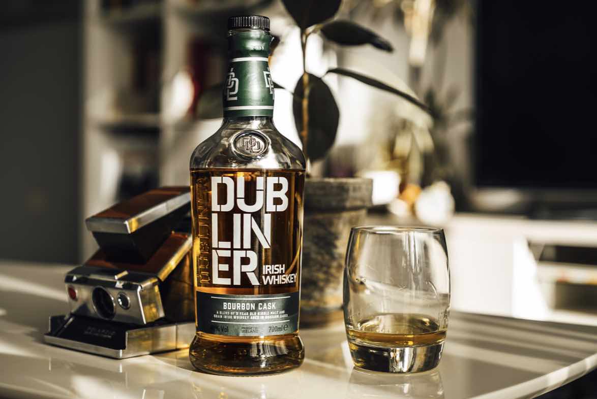 The Dubliner whisky bottle styled alongside a green plant in a plant pot and a crystal clear glass.