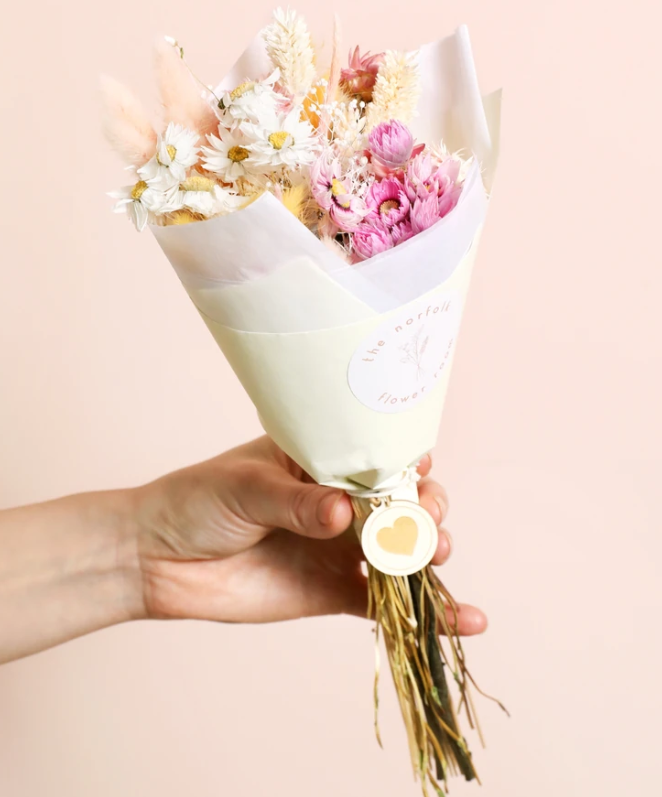 Blush and neutral pink toned faux flower bouquet with cream paper packaging, held in a lady's hand for display
