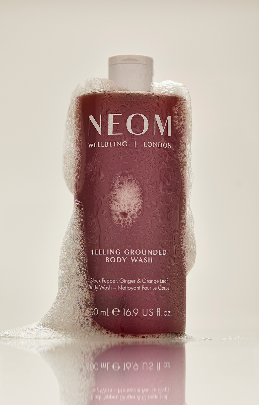 Neom body wash bottle with foamy soap suds on the side