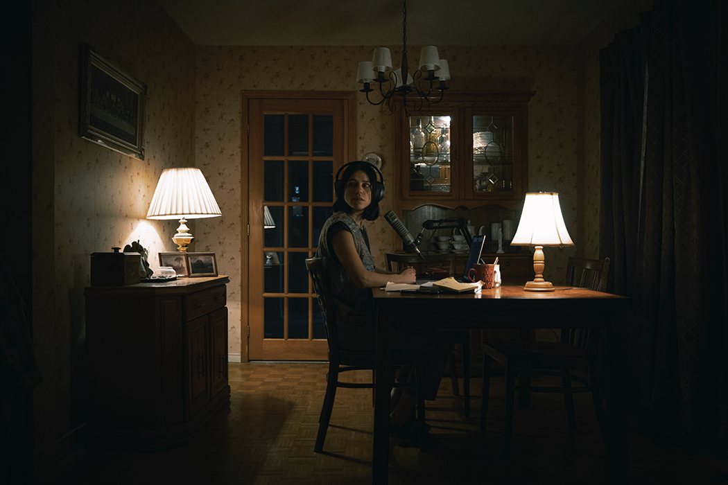 Woman sat to desk, low lighting, looking nervously behind her.