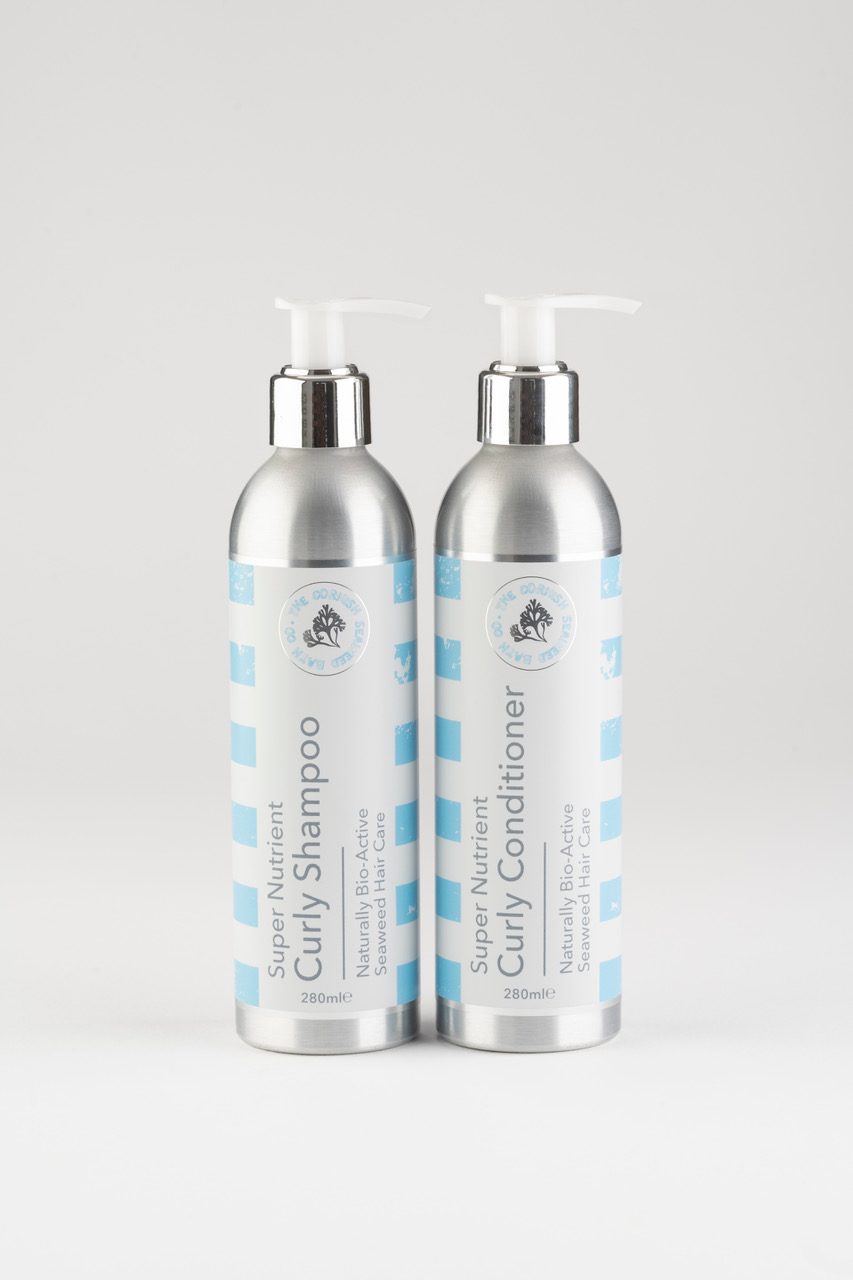 Curly hair shampoo in silver packaging with white lids against a grey backdrop