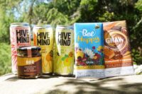Products for world bee day lined up in a row against a green leafed tree.