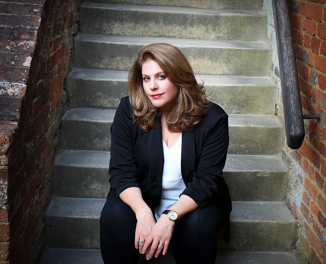 Author Ava Glass sat on grey steps wearing a fitted suit